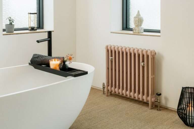 Castrads Mercury cast iron radiator under window in bathroom painted in pastel pink.