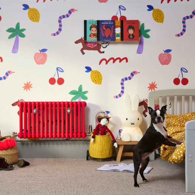 Lifestyle photo of strawberry red Florence steel column radiator in children's bedroom.