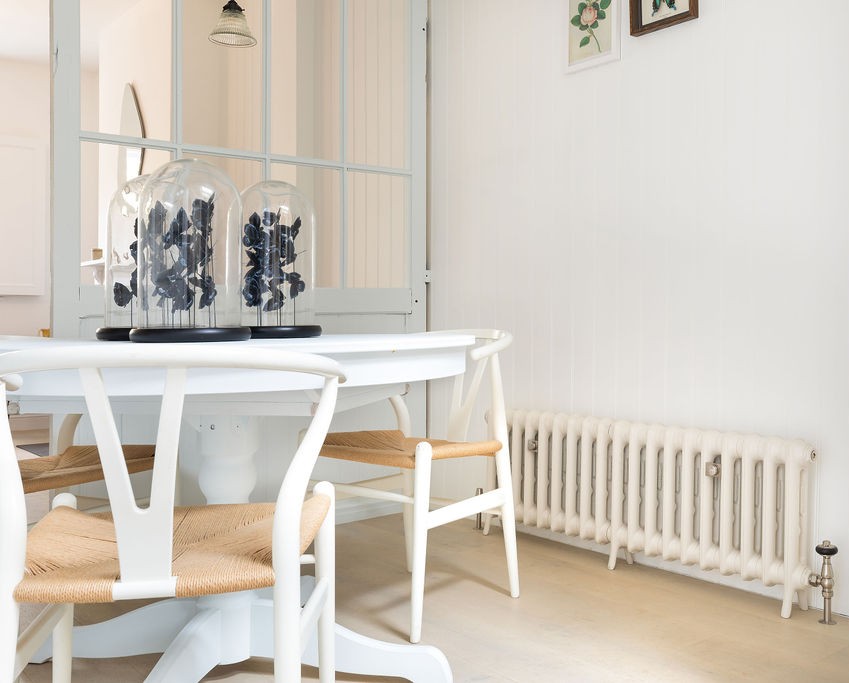 A dining room table and chairs beside a Castrads cast iron radiator in Farrow & Ball Ammonite in a home in Putney, South West London