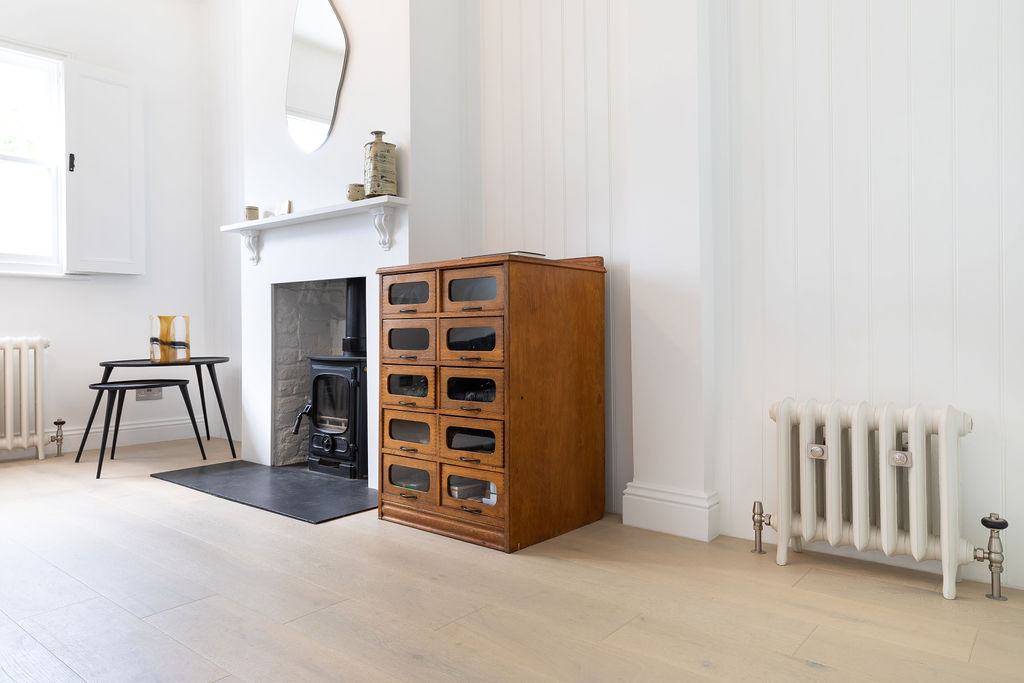 Living room with antique chest of drawers and cast iron stove with Castrads cast iron radiators in Farrow & Ball Ammonite in a home in Putney, South West London